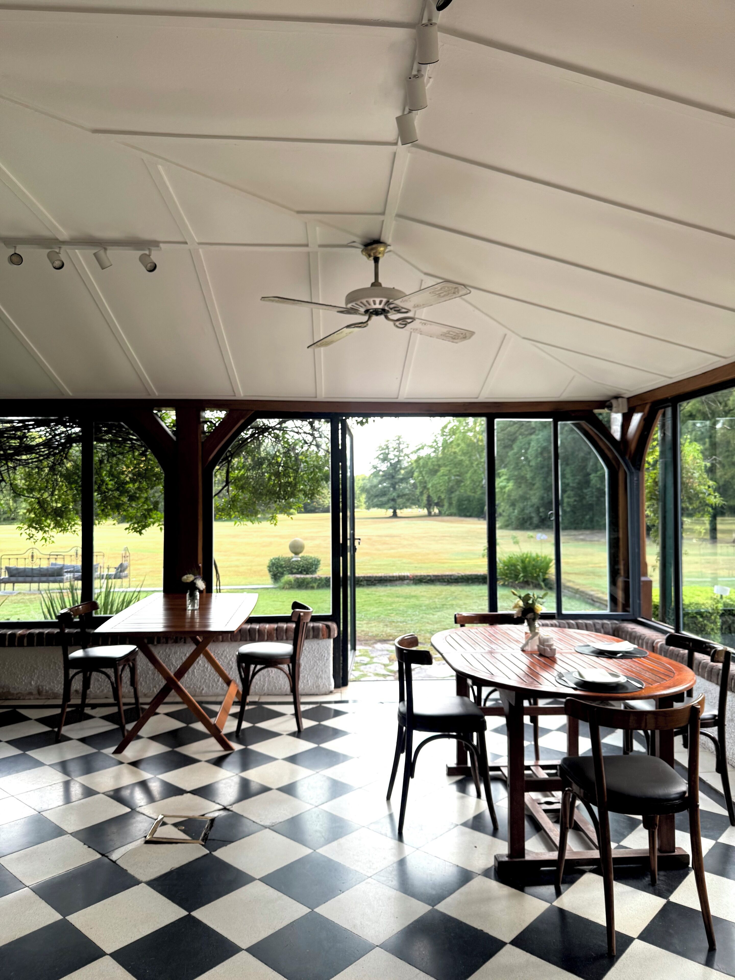 Un patio cubierto con suelo de cuadros, una mesa dispuesta para comer y vistas a un paisaje verde a través de amplios ventanales.