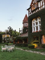 Uma casa tradicional de enxaimel com paredes cobertas de hera, uma torre com telhado vermelho e um jardim com uma mesa e cadeiras de metal branco.