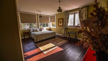 A bedroom with a bed, a nightstand, a window with curtains, a wooden floor, and a red side table.
