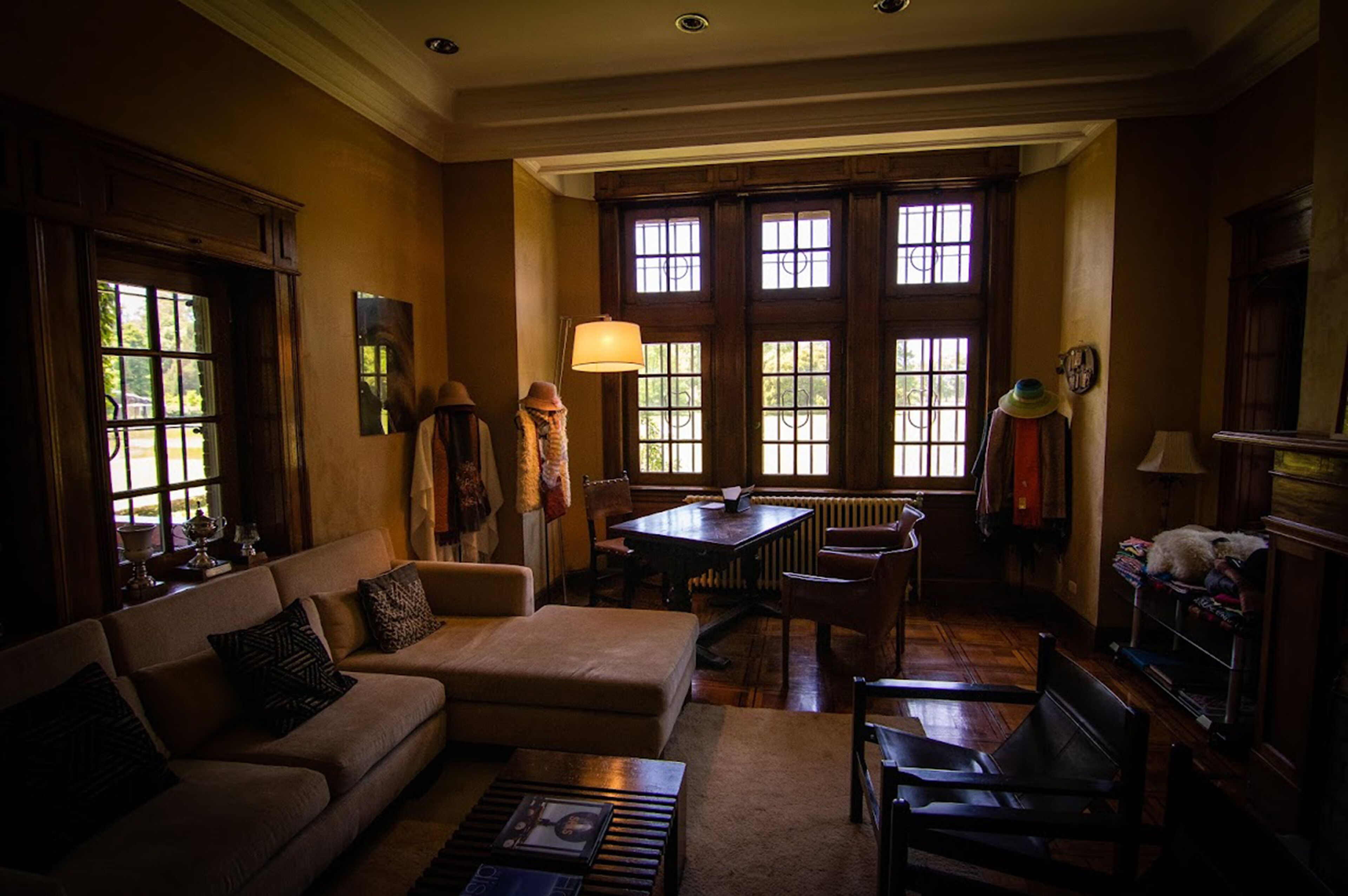 A cozy living room with a sofa, armchair, and a table. Large windows allow natural light to fill the space.