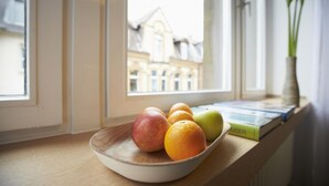 A wooden bowl with fruits on a windowsill, a book, and a plant. - Aparthotel TU-TU (Essen)