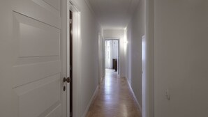 Un passadís amb parets blanques i terres de fusta, que condueix a una porta al final.