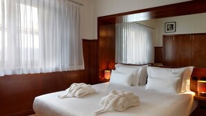 Habitació d'hotel amb un llit gran, dues tovelloles blanques, un panell de capçal de llit de fusta, làmpades de nit i un quadre al mur.