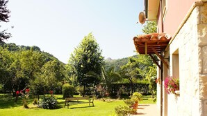 A garden with a bench, potted plants, and a building with a stone facade. - Casa Marian (Parres)