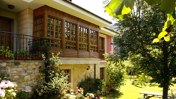 A house with a stone facade, large windows, and a garden with flowers and a picnic table. - Casa Marian (Parres)