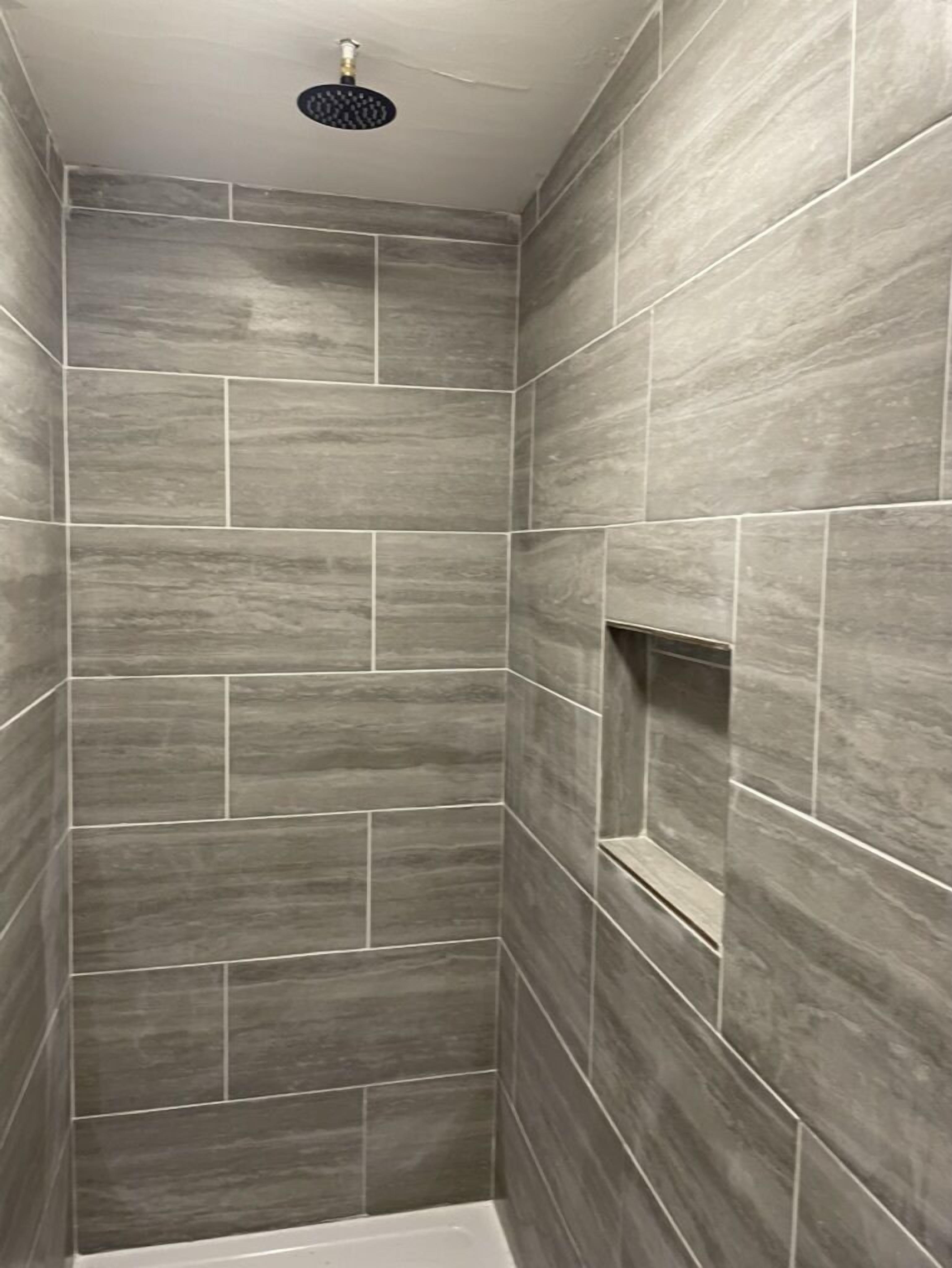 A shower with grey tiles and a showerhead.