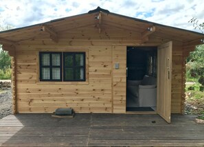 Une cabane en bois avec une seule fenêtre et une porte donnant sur un intérieur aménagé avec un canapé.