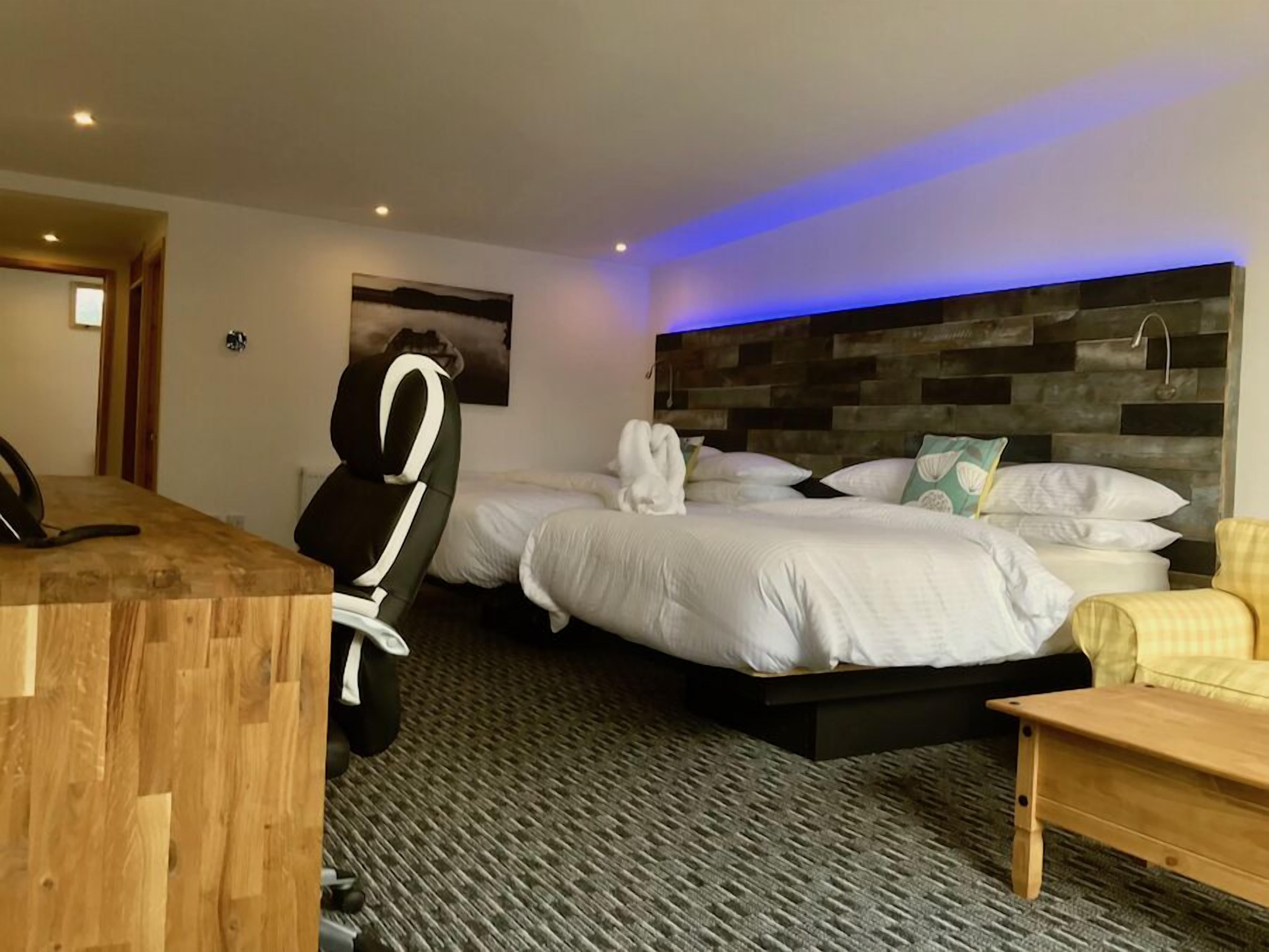 Ein Hotelzimmer mit zwei Betten, einem Schreibtisch, einem Stuhl und einem hölzernen Kopfteil.