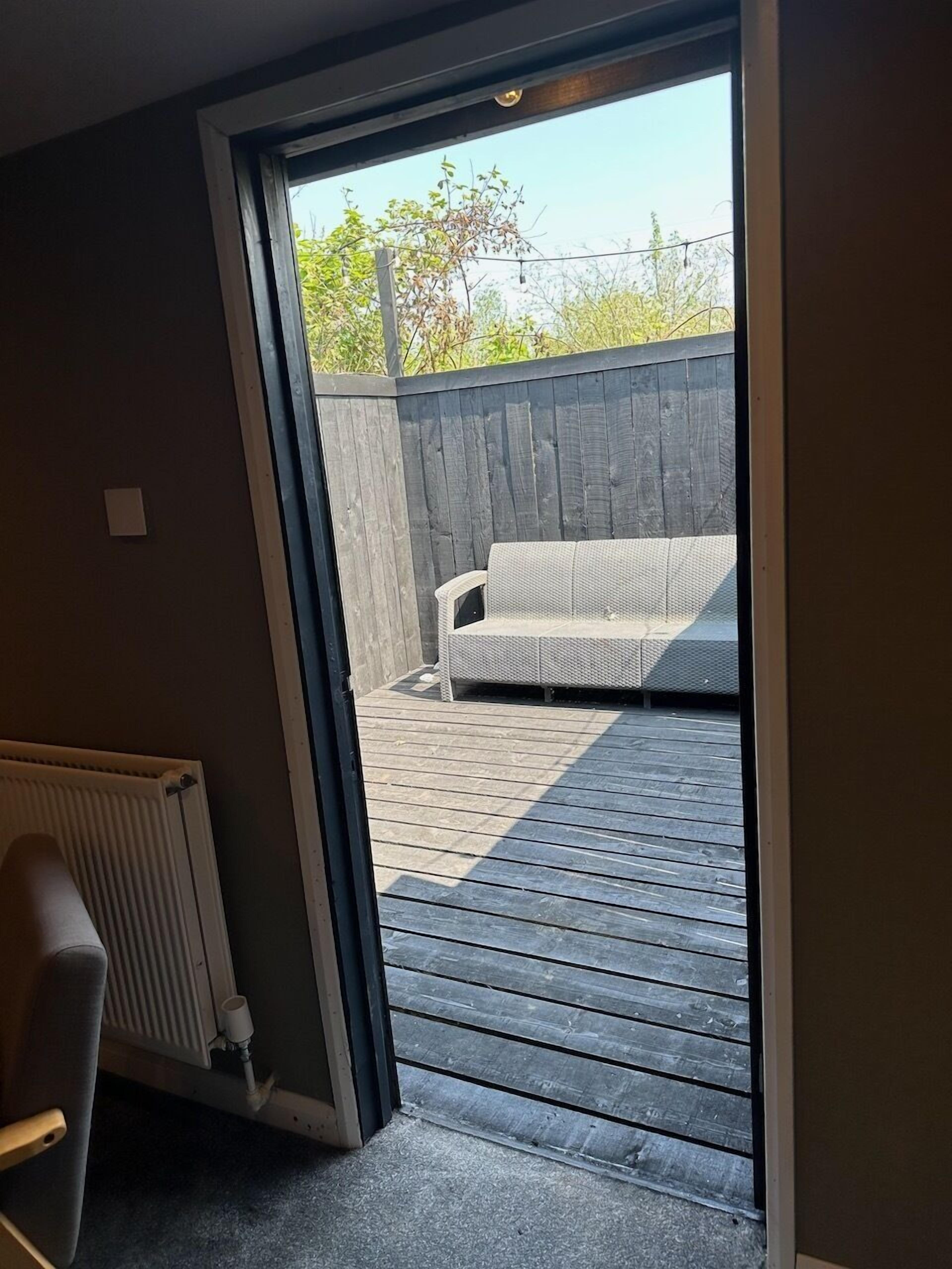 Puerta corredera abierta que da a un patio con un sofá y una terraza de madera.
