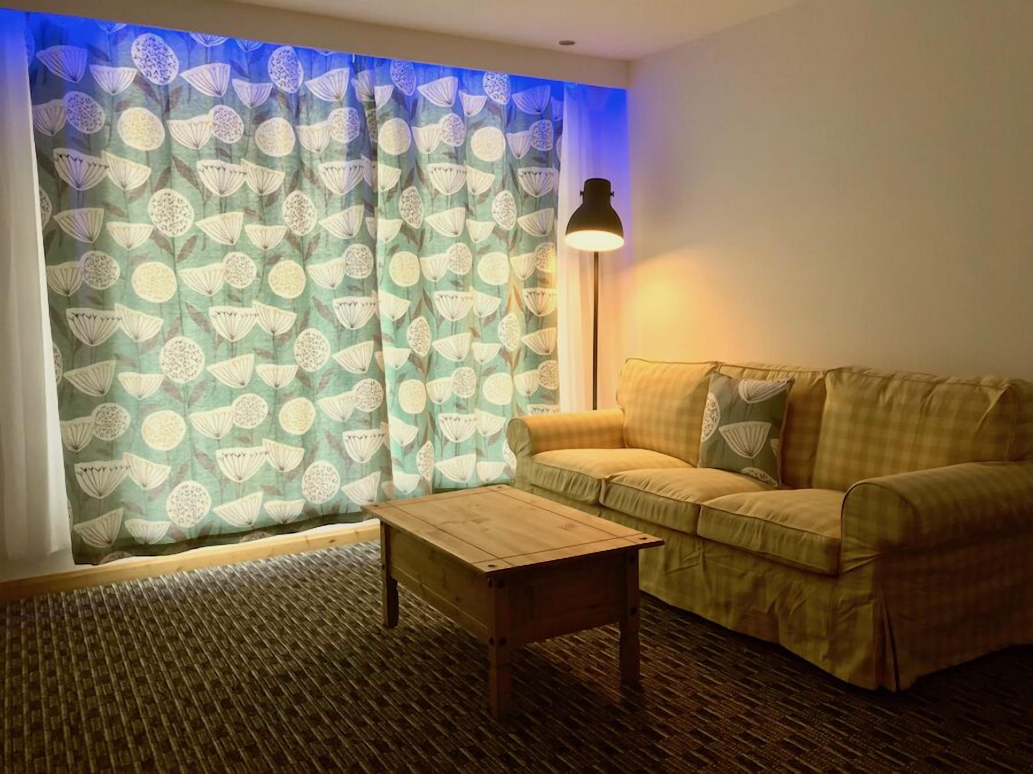 Una sala acogedora con una cortina estampada, un sofá, una mesa de centro de madera y una lámpara de pie.