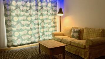 Una sala acogedora con una cortina estampada, un sofá, una mesa de centro de madera y una lámpara de pie.