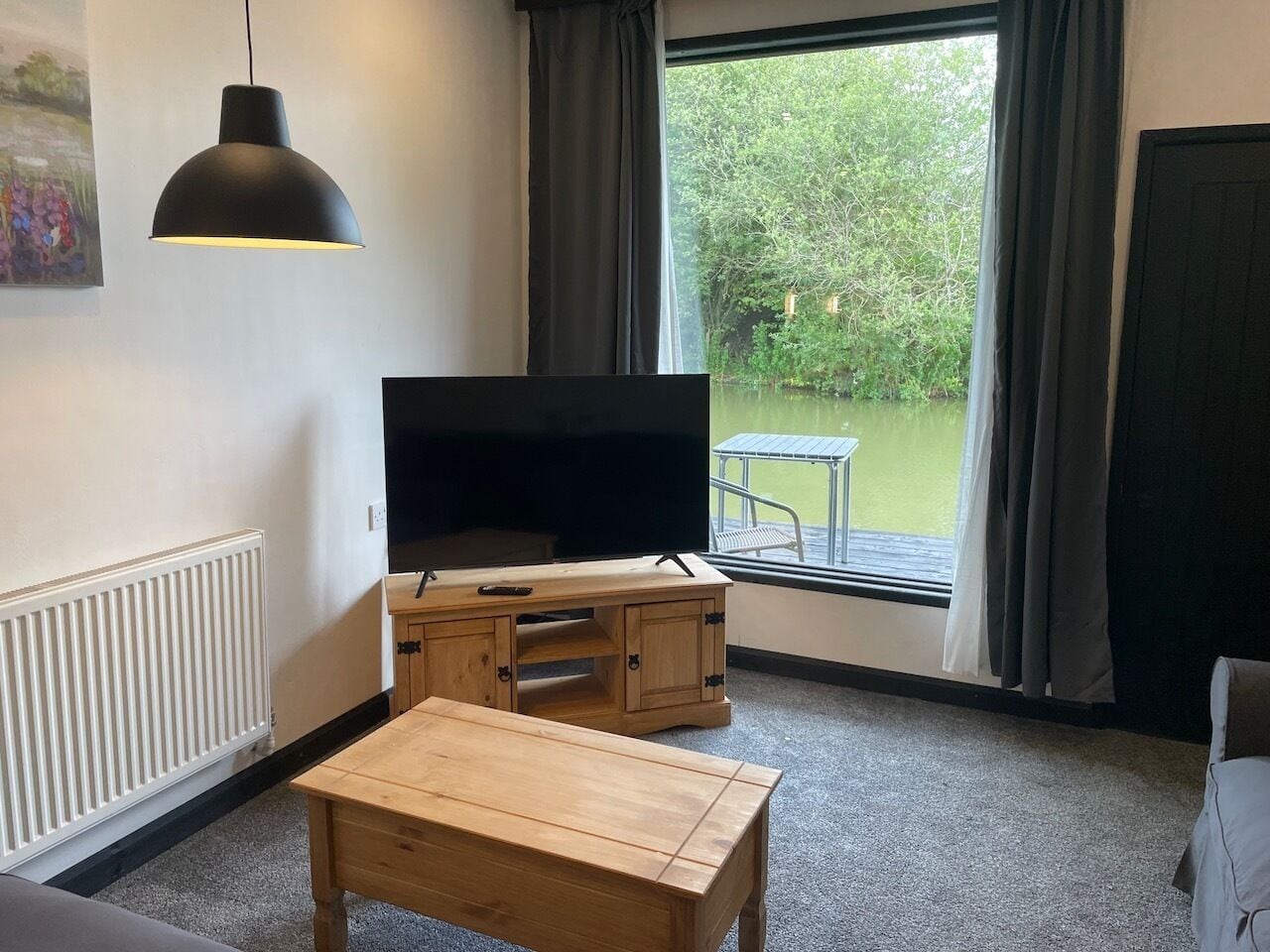Una sala de estar con televisor, mueble de madera y ventana con vista a follaje.