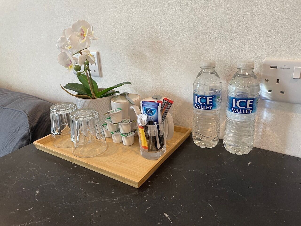A tray with a white orchid, a glass pitcher, and two bottles of Ice Valley water on a dark countertop.