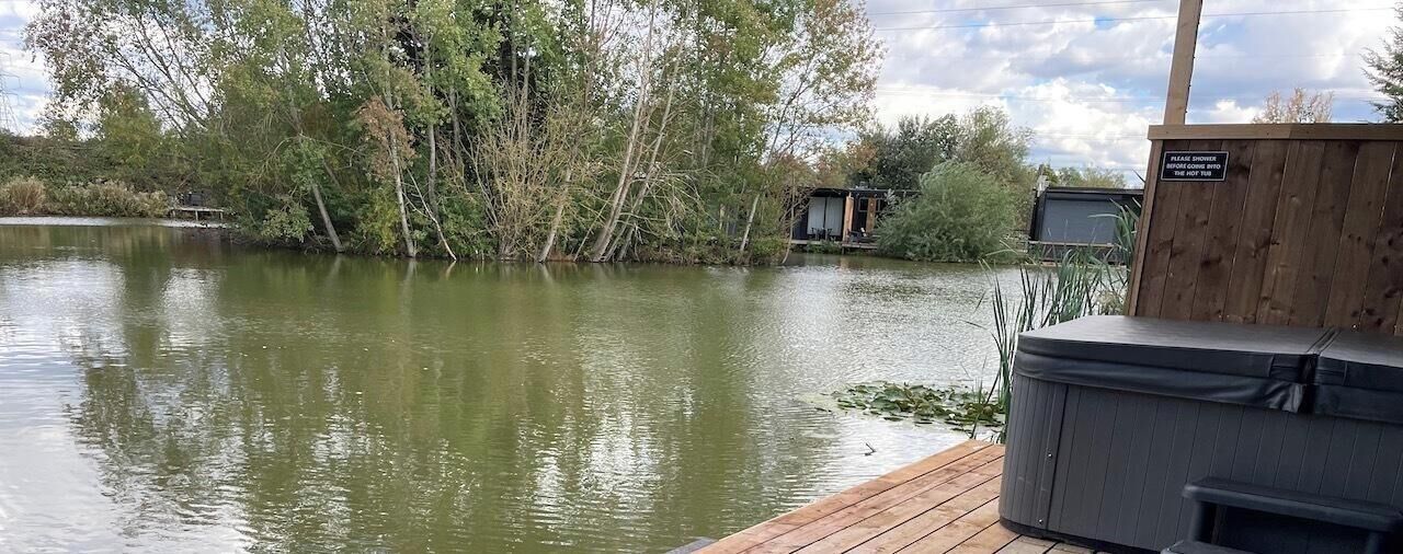 A wooden dock extending into a calm lake, surrounded by trees and a small building.