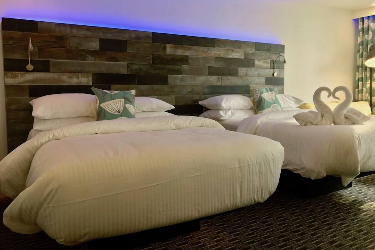 A hotel room with two beds, a wooden headboard, and a blue-lit ceiling.