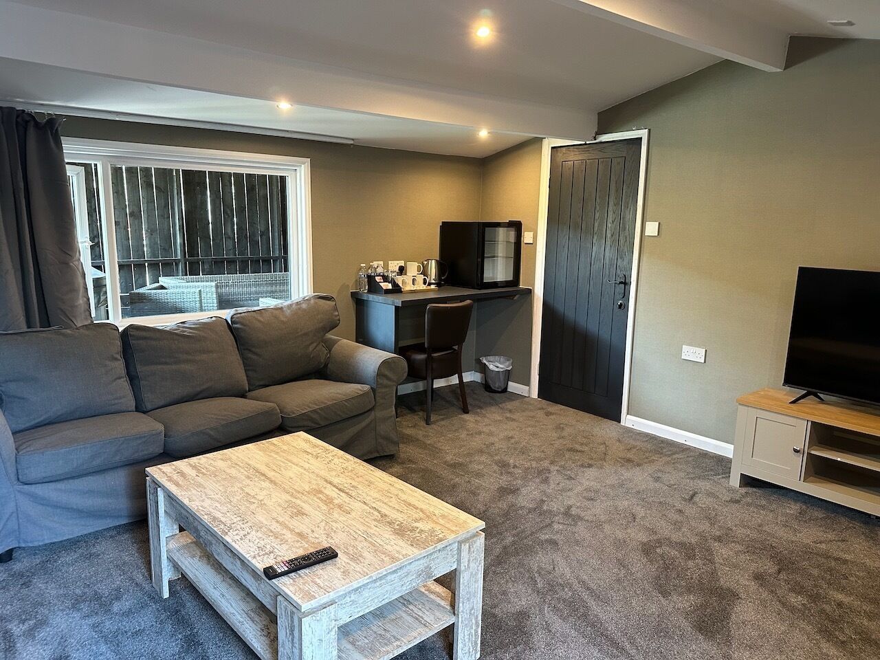 A living room with a grey sofa, a wooden coffee table, a TV stand, and a small desk with a chair.