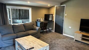 A living room with a grey sofa, a wooden coffee table, a TV stand, and a small desk with a chair.