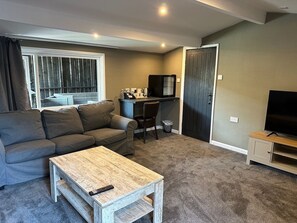 Un salon avec un canapé gris, une table basse en bois, un meuble pour la télévision et un petit bureau avec une chaise.