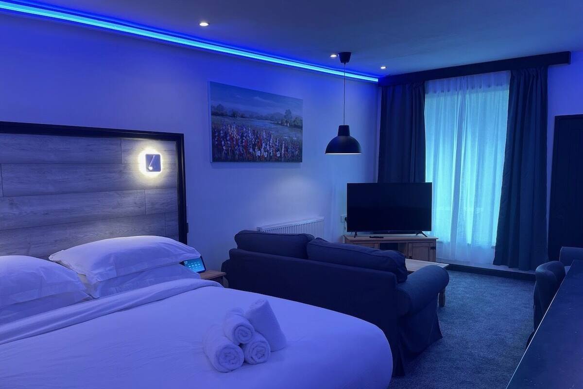 A modern hotel room with a large bed, a sofa, a TV, and a painting on the wall.