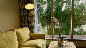Una habitación con un sofá amarillo a cuadros, una mesa de centro de madera con una botella de vino y una copa, y vistas a un lago a través de amplios ventanales.