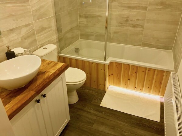 A bathroom with a wooden vanity, a white sink, a toilet, and a glass-enclosed shower area. - The Waterfront Lodges (Bedworth)