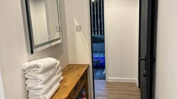 Un pasillo con un banco de madera, una pila de toallas blancas, un espejo y una puerta que da a un balcón.
