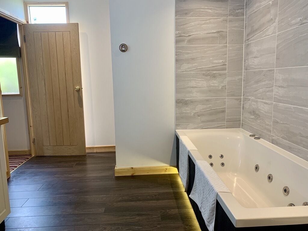 A bathroom with a large bathtub, wooden door, and tiled walls.