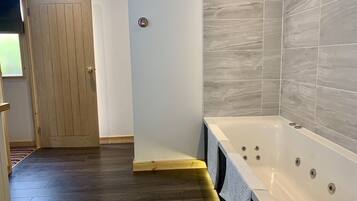 A bathroom with a large bathtub, wooden door, and tiled walls.
