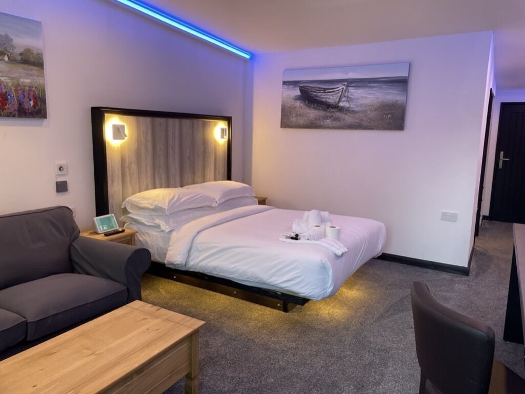 A modern hotel room with a bed, a sofa, a wooden table, and a painting on the wall.