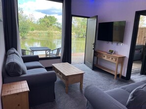 Une pièce comprenant un canapé, une table basse, un téléviseur et donnant sur un lac.