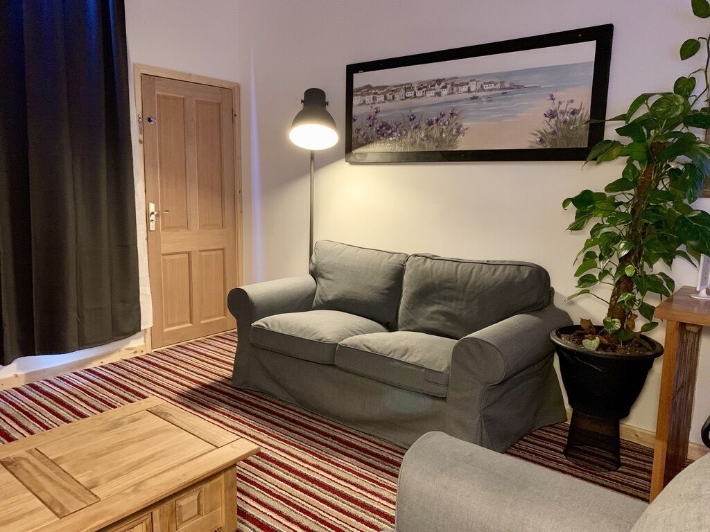 A living room with a grey sofa, a wooden coffee table, a black floor lamp, a framed picture on the wall, and a potted plant.