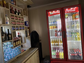 A vending machine stocked with beverages and a shelf with bottled water and alcohol.