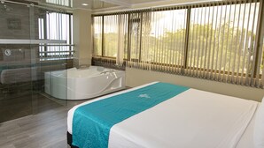 A modern hotel room with a large bed, a separate shower area, and a view of greenery outside. - Hotel Campo Real (Marinilla)