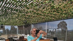 A person taking a selfie in a modern, well-lit outdoor dining area with a wooden floor, metal tables, and chairs. - Hotel Campo Real (Marinilla)