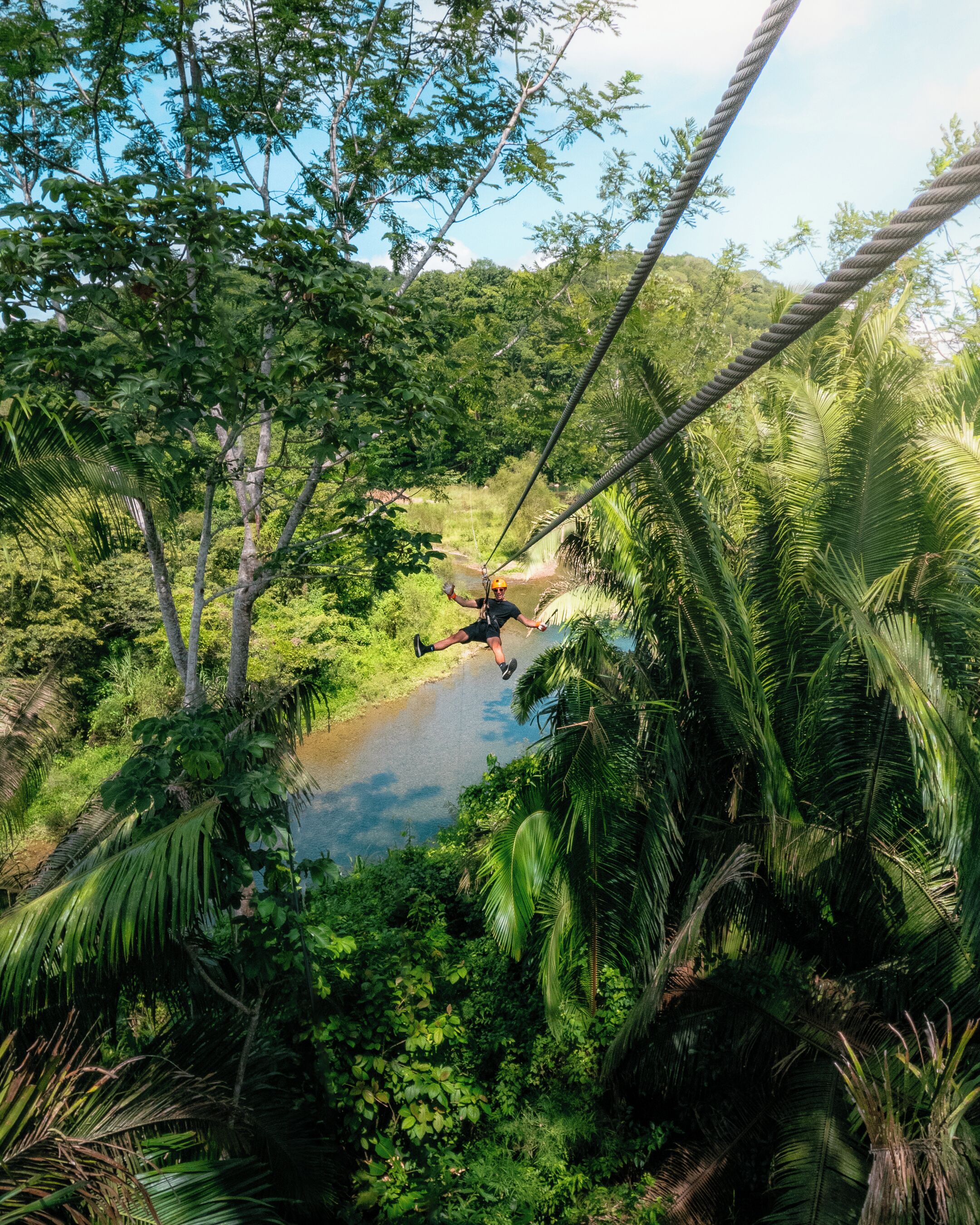 A zip line over a river surrounded by dense tropical foliage.