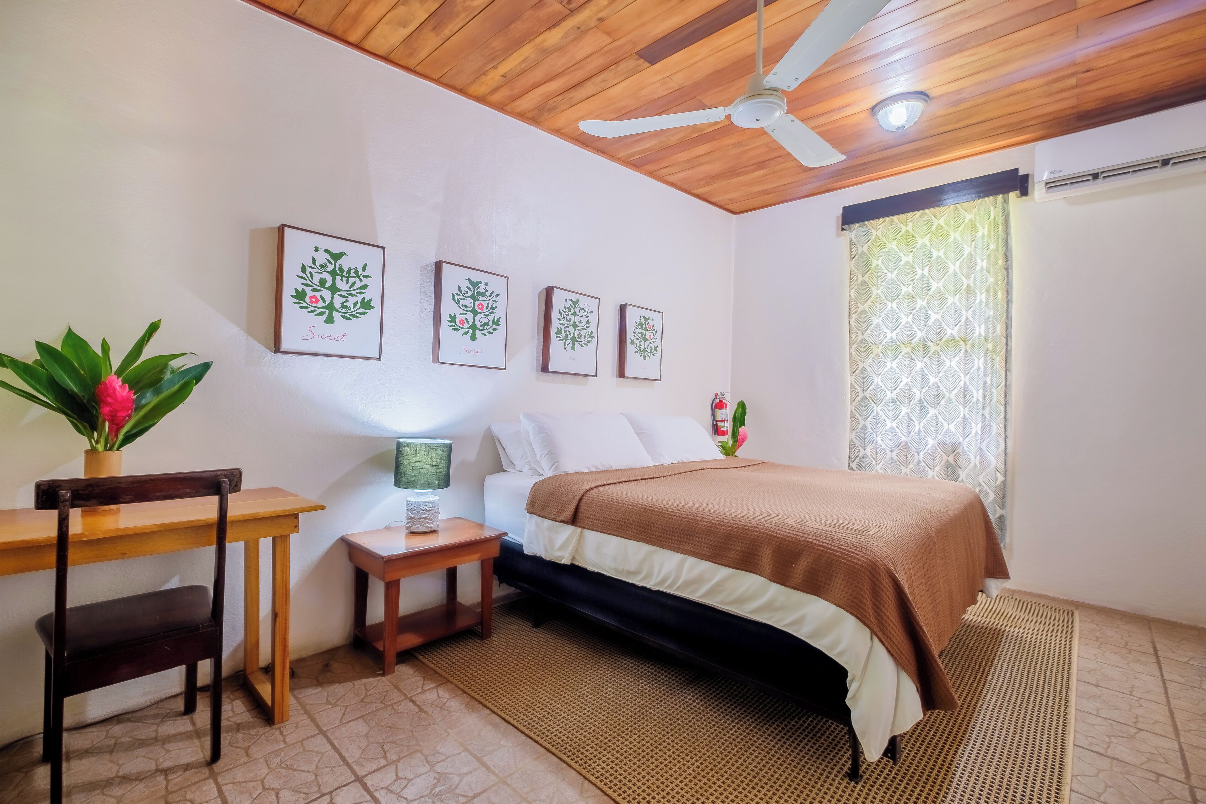 A bedroom with a bed, a desk, a chair, a ceiling fan, and wall-mounted artwork.