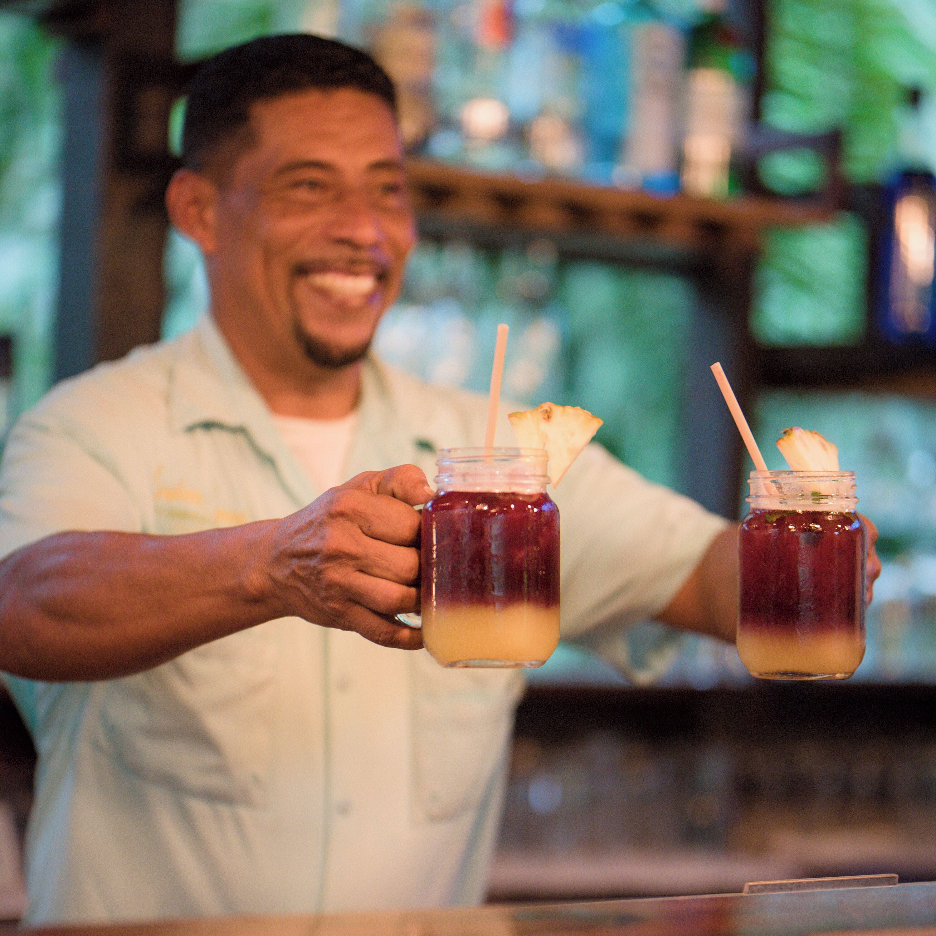 A person holding two drinks with straws, one with a pineapple slice.