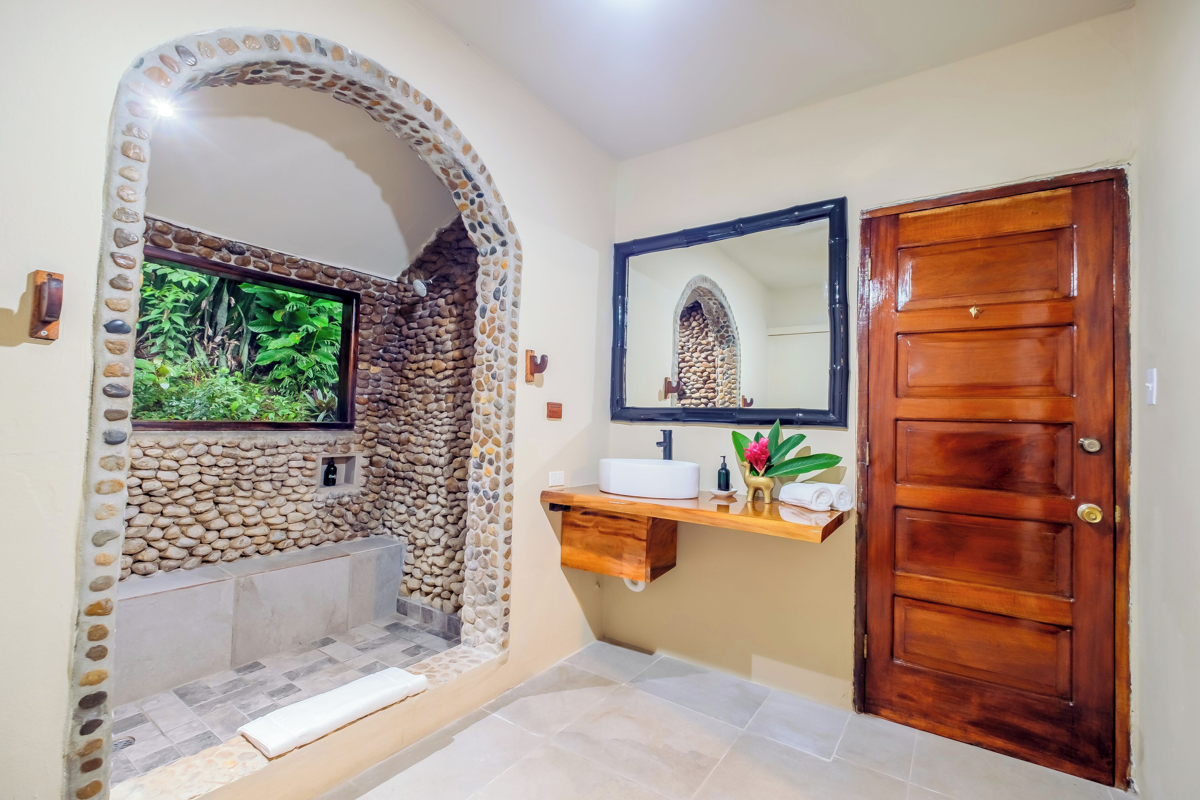 A bathroom with a stone wall, a wooden door, a sink, and a mirror.