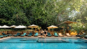 Piscina con sillones de descanso y sombrillas, rodeada de abundante vegetación.