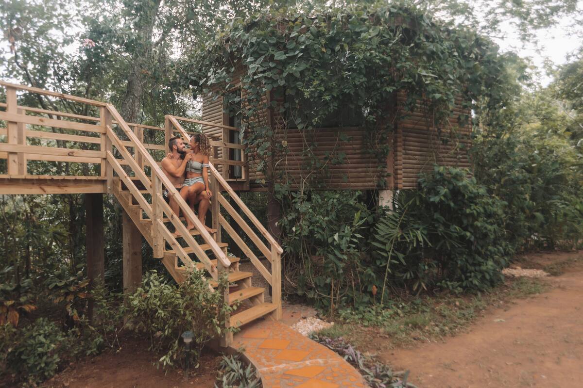 Een houten trap naar een eenvoudige chalet, omgeven door weelderige begroeiing.