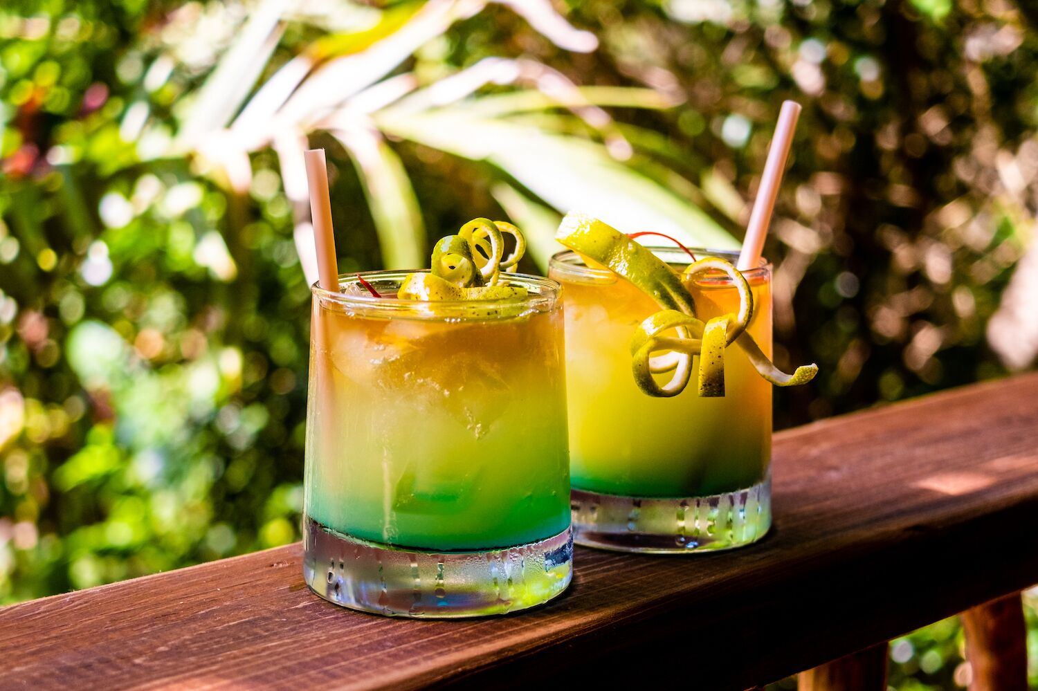 Dos vasos de bebidas en capas con pajitas y rodajas de limón sobre una superficie de madera.
