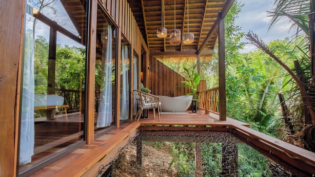 Una terraza de madera con una bañera, una silla y una mesa, con vistas a un jardín exuberante.