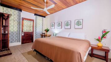 A bedroom with a wooden ceiling, a bed with a brown bedspread, a nightstand with a vase, and framed pictures on the wall.