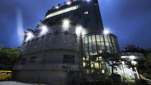 A modern hotel with a curved facade, multiple balconies, and a prominent water tower. - Jumunjin Hotel (Gangneung)