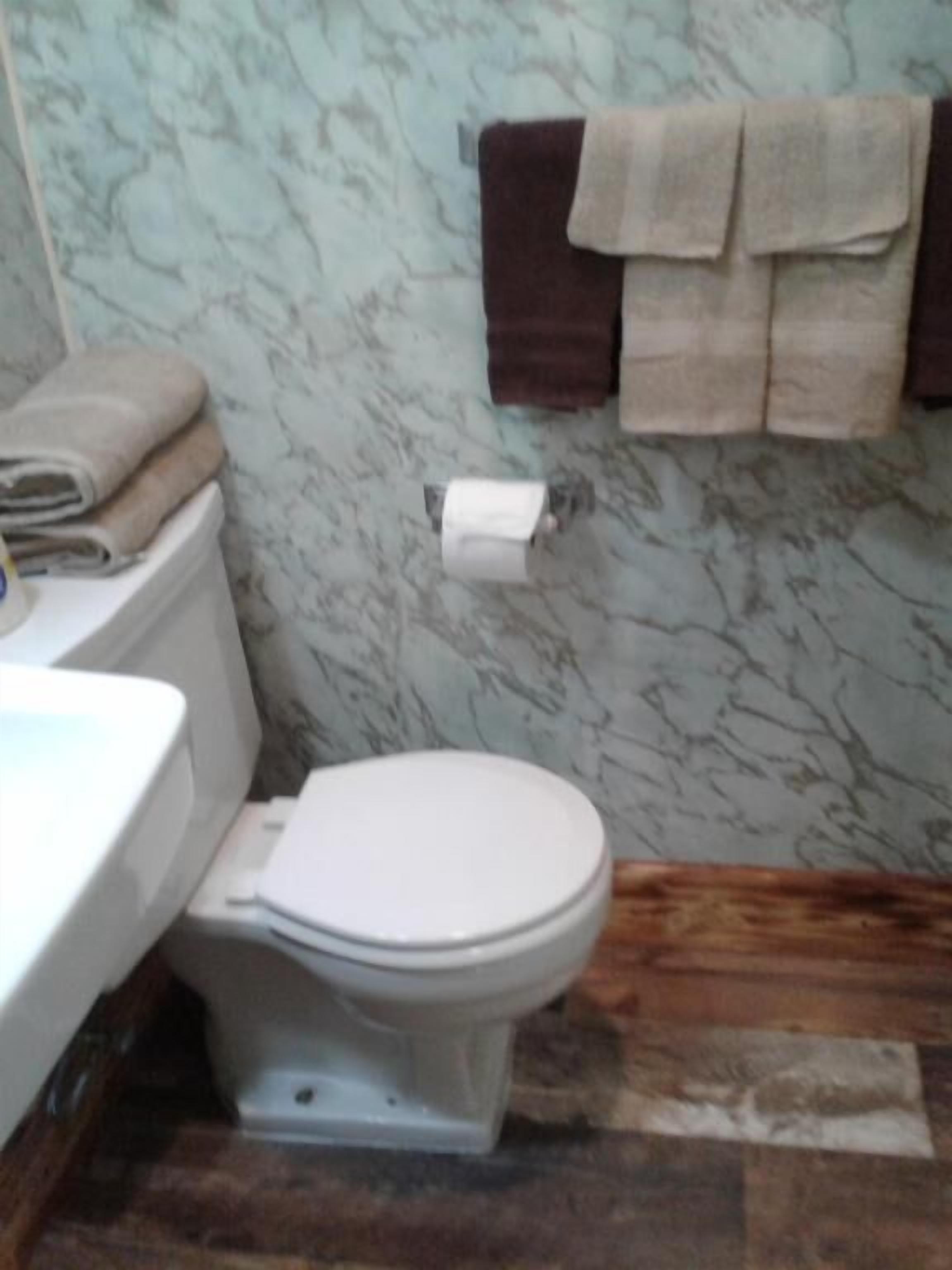 A bathroom with a toilet, a sink, and a marble wall. There are towels hanging on a rack.