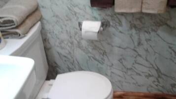 A bathroom with a toilet, a sink, and a marble wall. There are towels hanging on a rack.