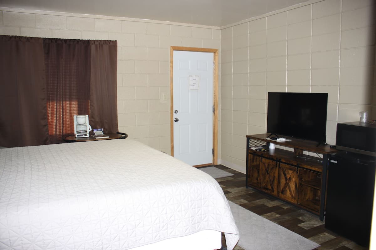 Quarto de hotel com cama, televisão, um pequeno armário e uma porta.