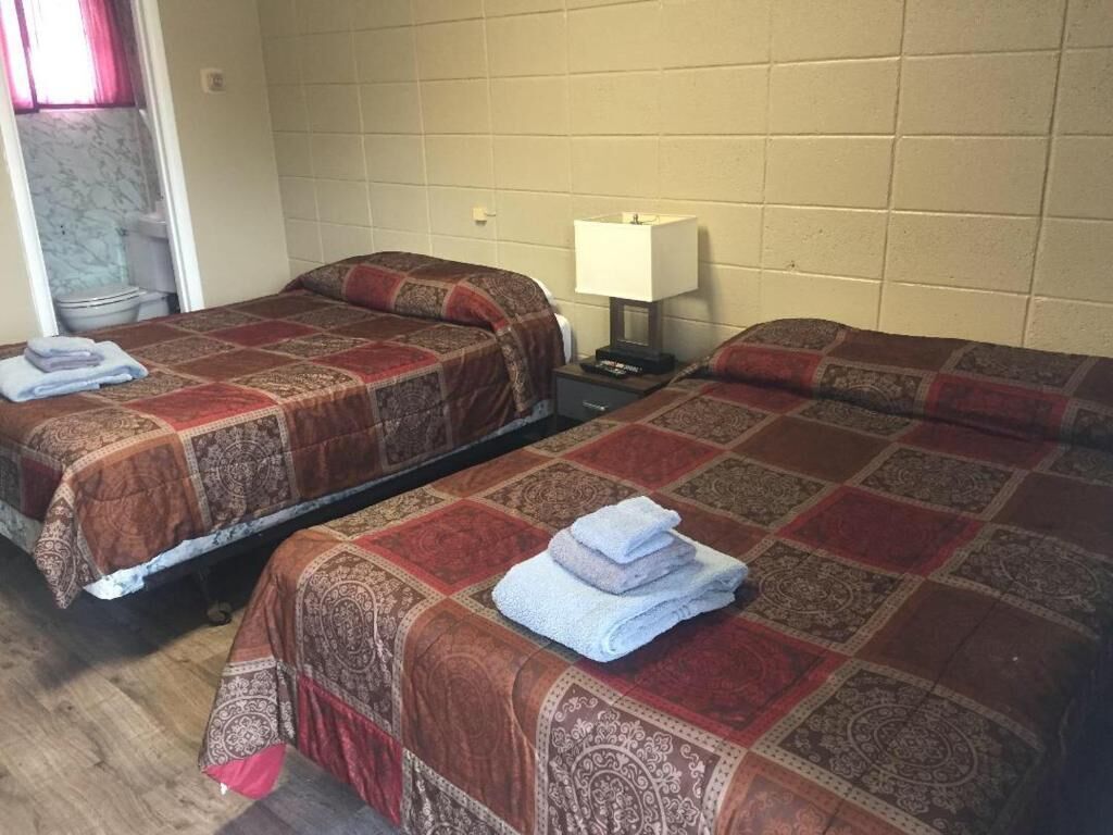 A room with two single beds, each with a patterned bedspread and a folded towel. There is a nightstand with a lamp between the beds.