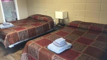 A room with two single beds, each with a patterned bedspread and a folded towel. There is a nightstand with a lamp between the beds.