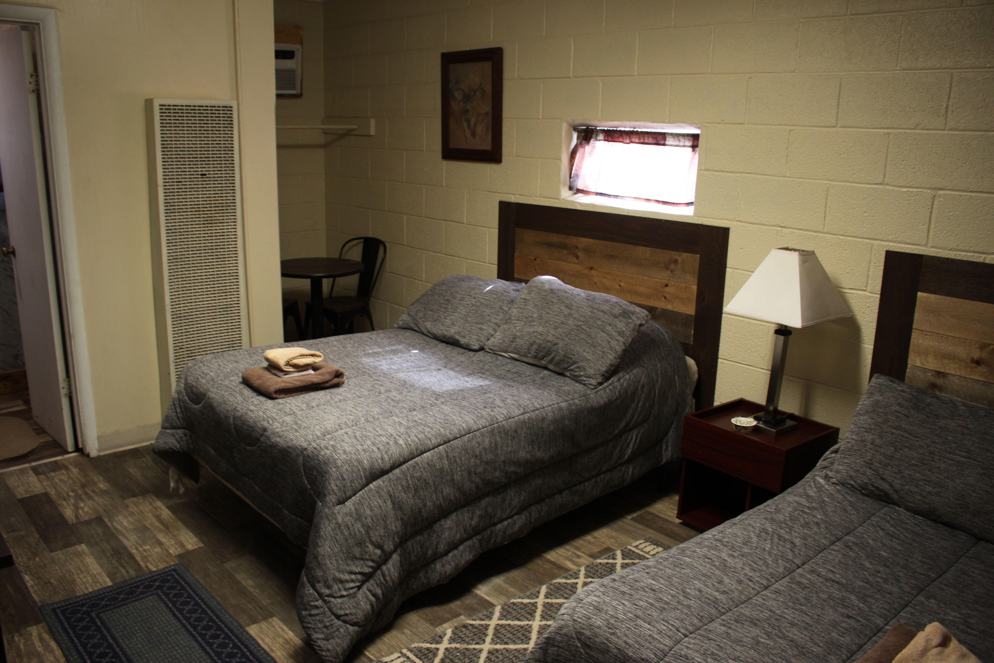 A bedroom with a single bed, a bedside table with a lamp, a chair, and a window with a curtain.